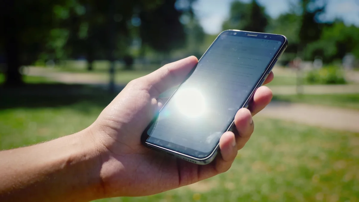 Mano sujetando un smartphone a pleno sol con la pantalla encendida